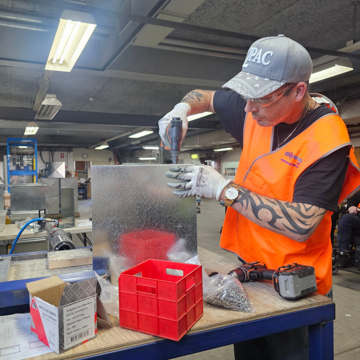 An employee is using a drill on a large metal box.